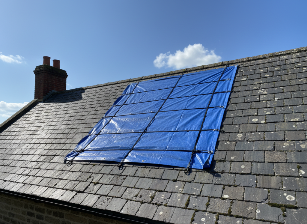 Blue tarpaulin strapped over a section of missing slates on a Kent roof as a temporary emergency cover