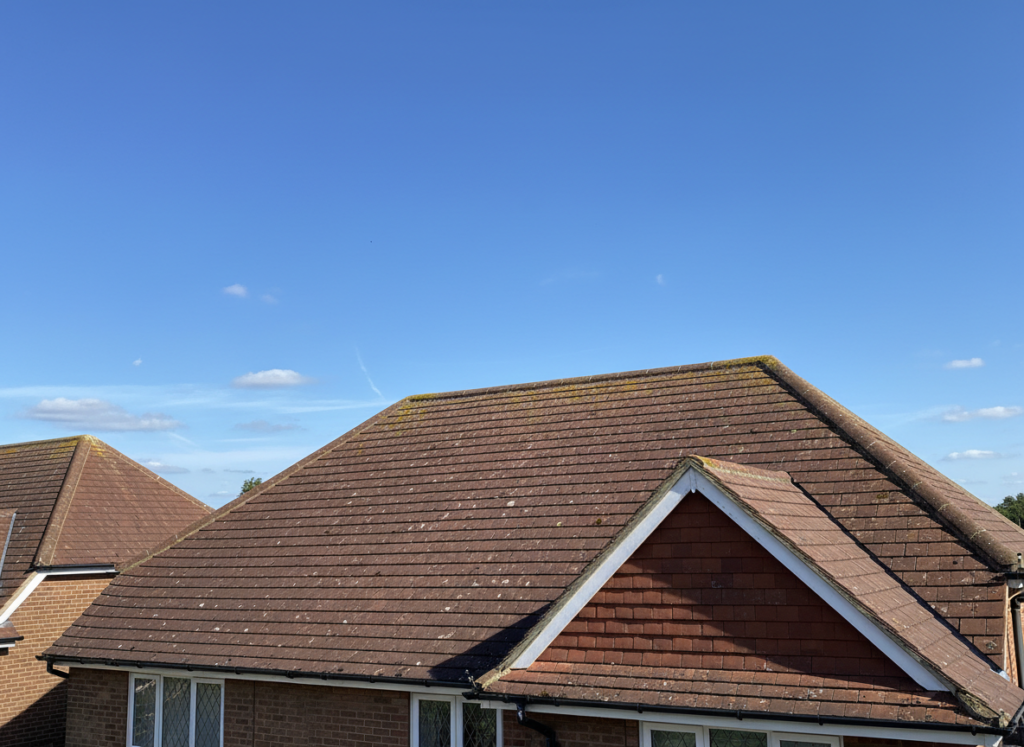 Whole pitched clay tile roof of a Kent house showing the hip, ridge and gable end against a bright blue sky