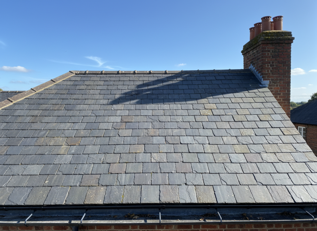 Elevated survey view across a complete Welsh slate roof showing the ridge, slate courses, chimney stack and gutter line