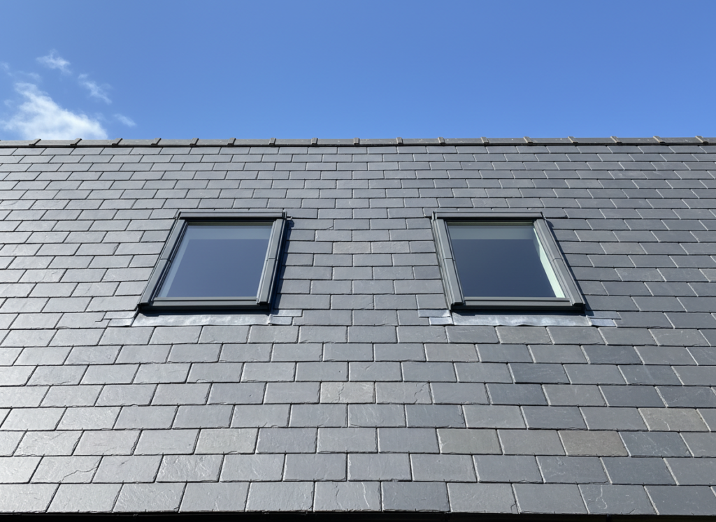 Two roof windows set into a grey slate pitched roof with lead flashing dressed neatly into the slates