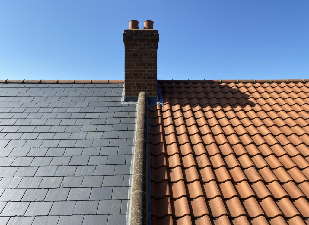 Blue grey Welsh slate roof meeting a terracotta clay pantile roof either side of a red brick chimney stack